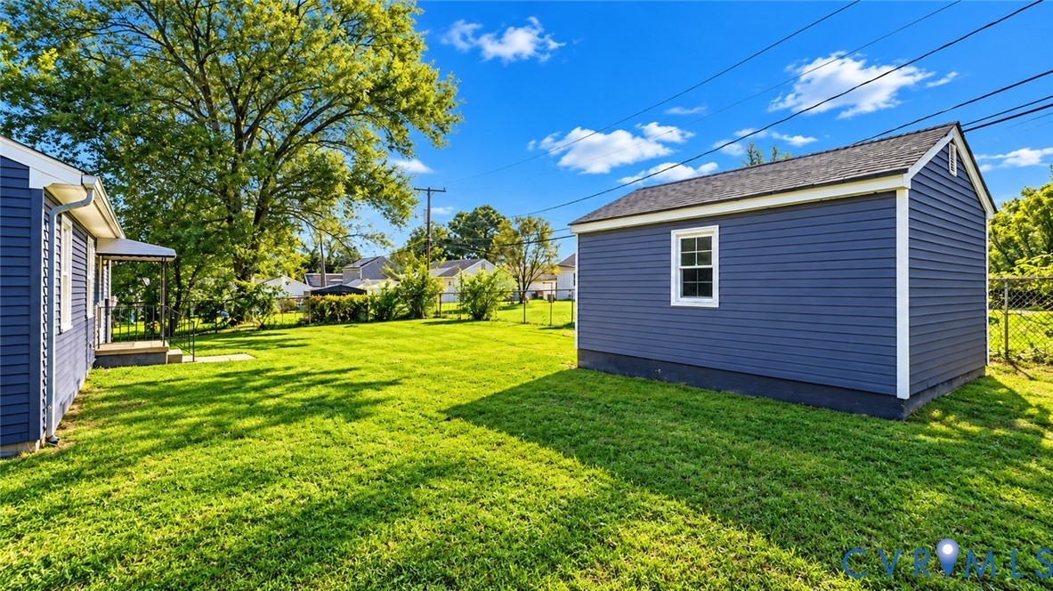 Spacious backyard featuring a manicured lawn, detached storage structure with blue siding, and chain-link perimeter fencing