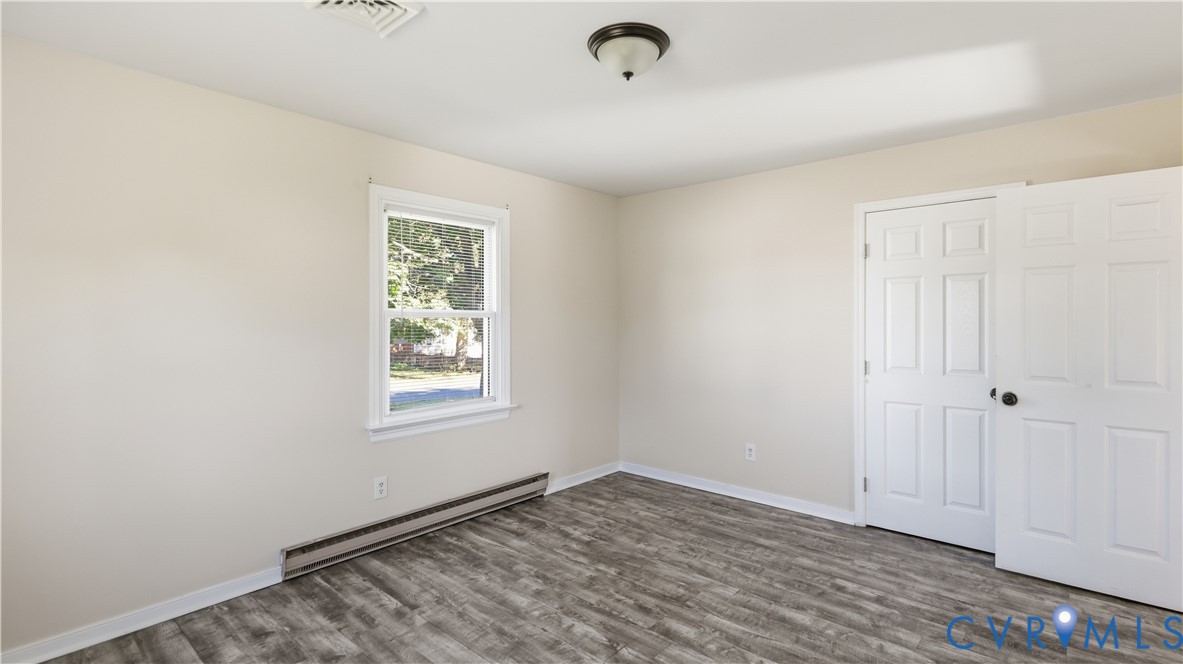 Room featuring wood-finish flooring, neutral-toned walls, six-panel interior door, and a single-hung window