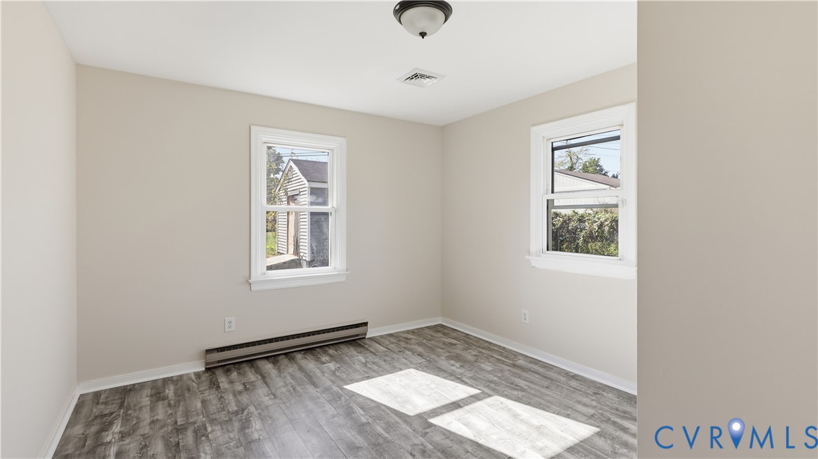 Neutral-toned walls, wood-finish flooring, two dual-pane windows with white trim, and a flush-mount ceiling light fixture