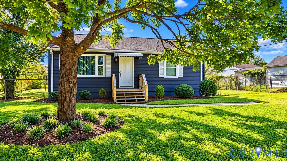 Dark blue siding exterior featuring white shutters, a covered front entry with wood-toned steps, and a landscaped front yard with a mature tree