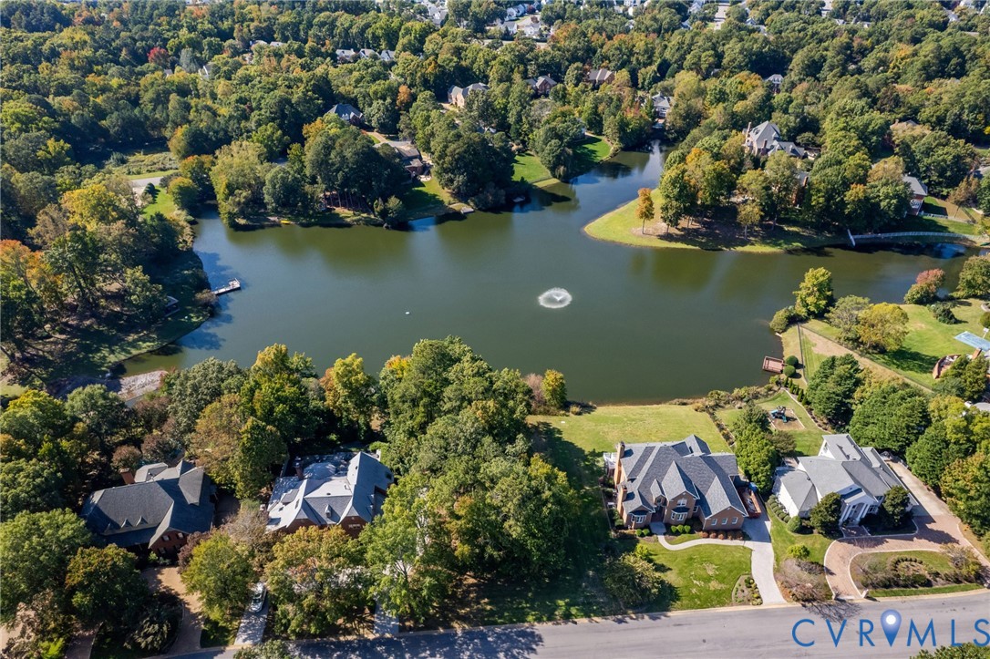 Aerial perspective of waterfront properties featuring expansive pond frontage, mature wooded landscape, and paved driveways