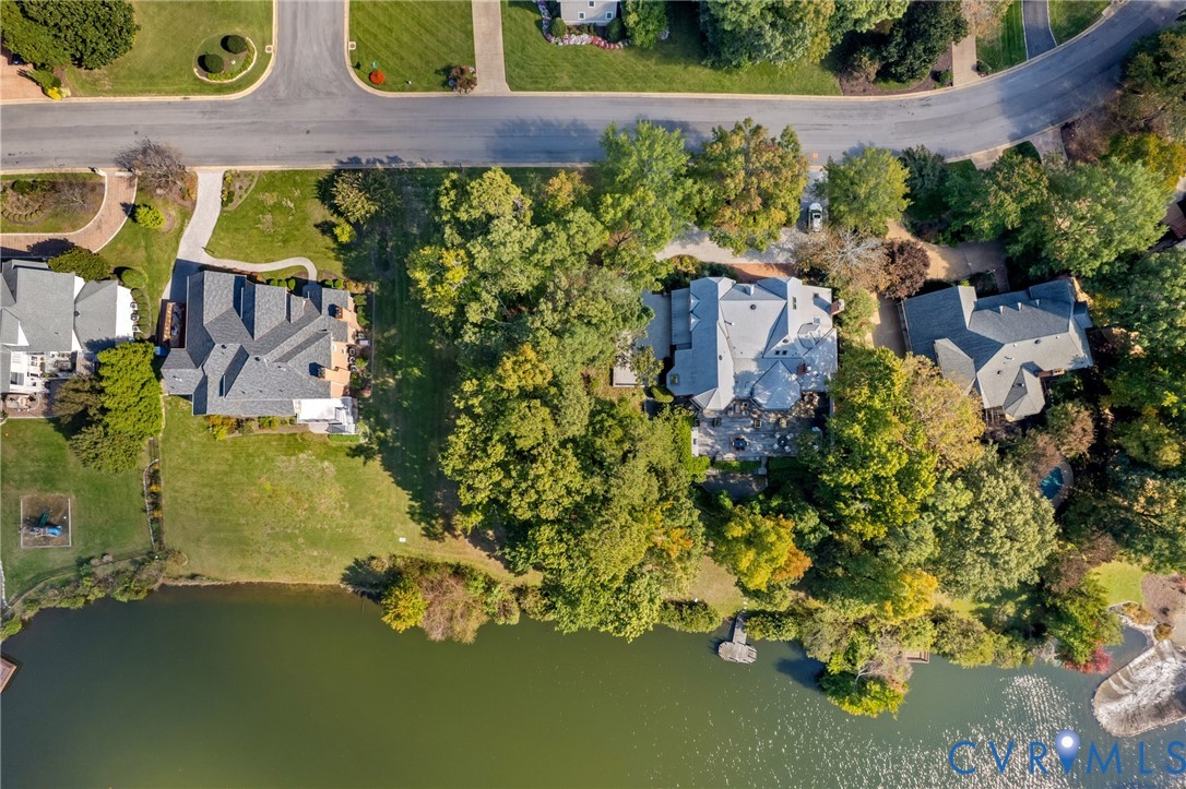 Aerial perspective featuring a waterfront property with extensive tree canopy, a paved driveway, and established landscaping