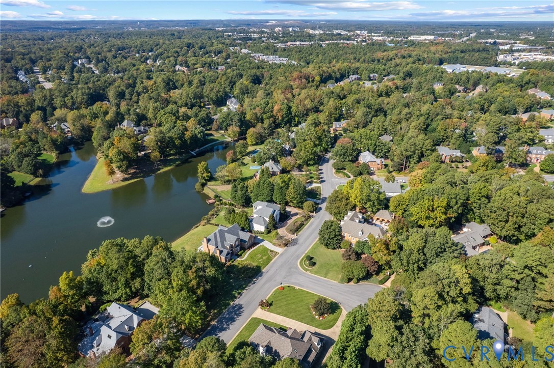 Aerial perspective of a residential neighborhood featuring mature canopy trees, winding asphalt roads, and a large central lake with a fountain