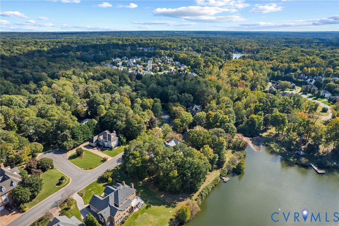 Aerial perspective featuring waterfront property, expansive wooded acreage, paved street infrastructure, and multiple detached residential structures