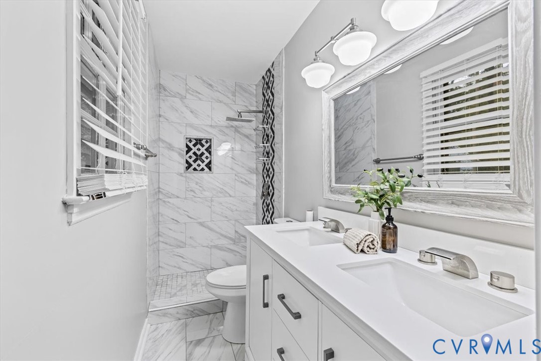 Dual-sink vanity with white countertop, stone-finish tile shower surround with geometric accent inlay, rainfall shower head, and wall-mounted vanity lighting Dual-sink vanity with white countertop, stone-finish tile shower surround with geometric accent inlay, rainfall shower head, and wall-mounted vanity lighting