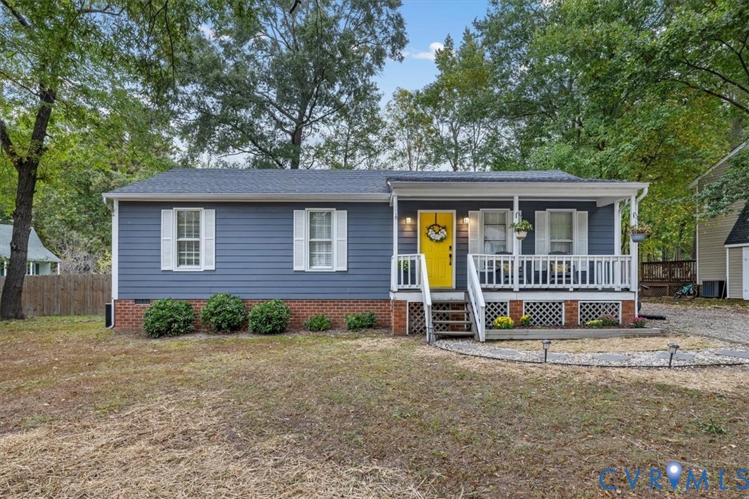 Exterior featuring blue horizontal siding, a red brick foundation, a covered front porch with white railing, and a vibrant yellow entry door