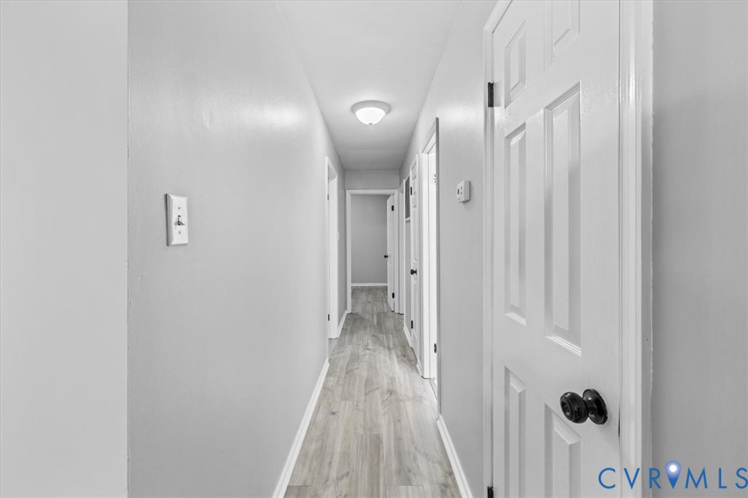 Hallway featuring wood-finish flooring, white six-panel doors, matte black hardware, and a flush-mount ceiling light fixture