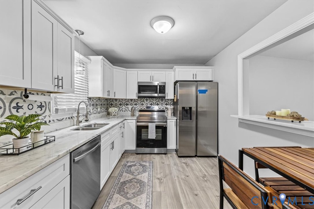 Kitchen featuring white cabinetry, patterned backsplash tile, stainless steel appliances, and wood-finish flooring