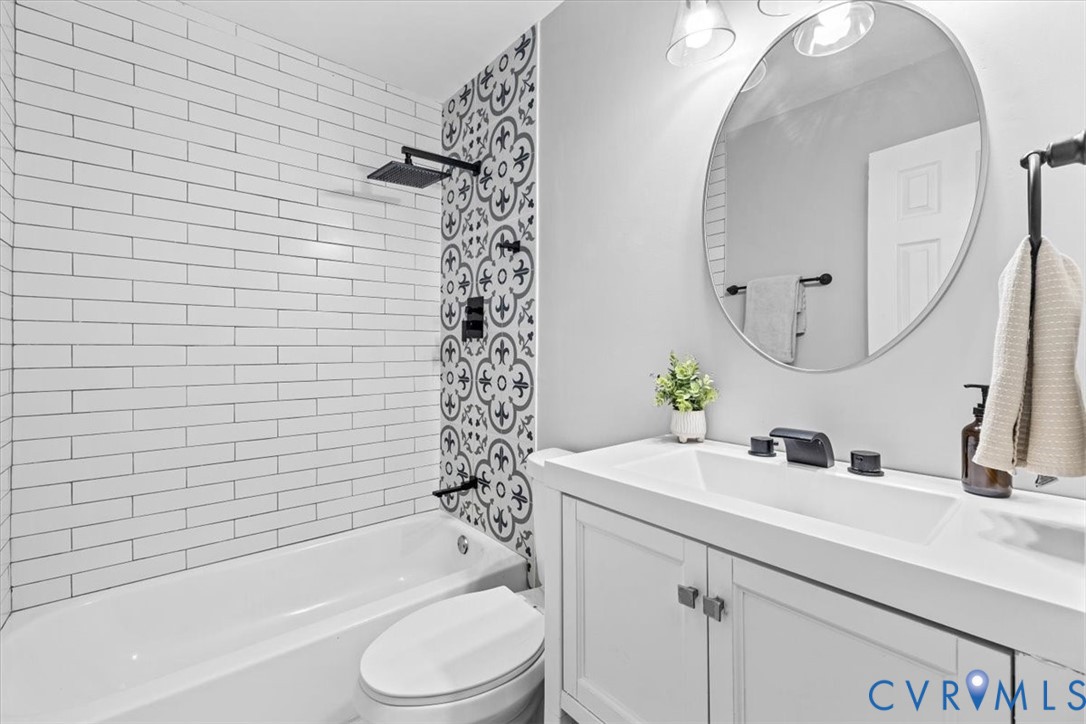 Bathroom featuring white subway tile, decorative patterned accent tile, matte black shower fixtures, vanity with an integrated sink, and an oval wall-mounted mirror Bathroom featuring white subway tile, decorative patterned accent tile, matte black shower fixtures, vanity with an integrated sink, and an oval wall-mounted mirror
