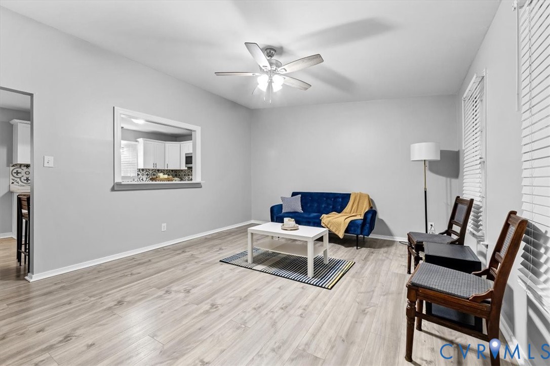 Neutral walls, wood-finish flooring, ceiling fan with integrated lighting, and a passthrough opening Neutral walls, wood-finish flooring, ceiling fan with integrated lighting, and a passthrough opening