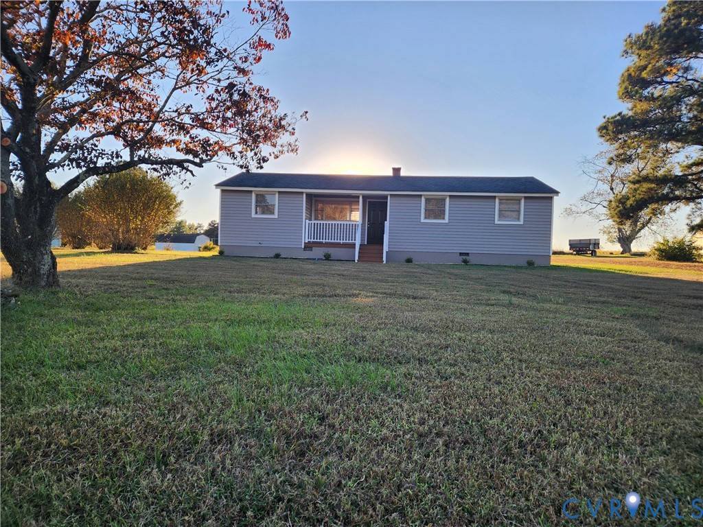 Single-story residence featuring light-toned horizontal siding, a covered front porch with white railing, and an expansive grass yard with mature trees Single-story residence featuring light-toned horizontal siding, a covered front porch with white railing, and an expansive grass yard with mature trees