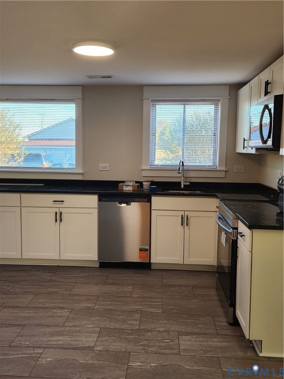 Kitchen featuring white Shaker-style cabinetry, dark stone-finish countertops, stainless steel appliances, and large-format tile flooring