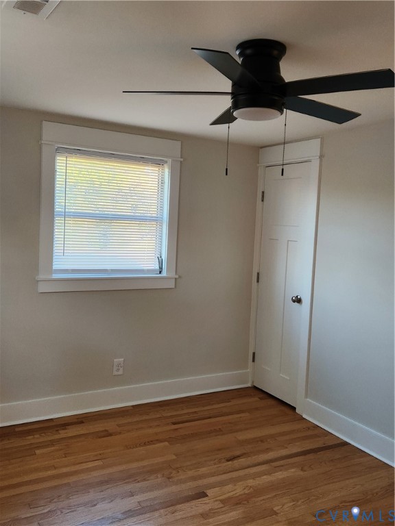 Interior space featuring wood-finish flooring, a multi-panel door, a window with decorative casing, and a black ceiling fan with an integrated light fixture