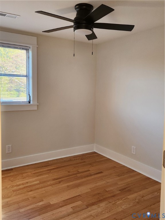 Room featuring wood-finish flooring, a multi-blade ceiling fan with integrated lighting, and a window with white trim