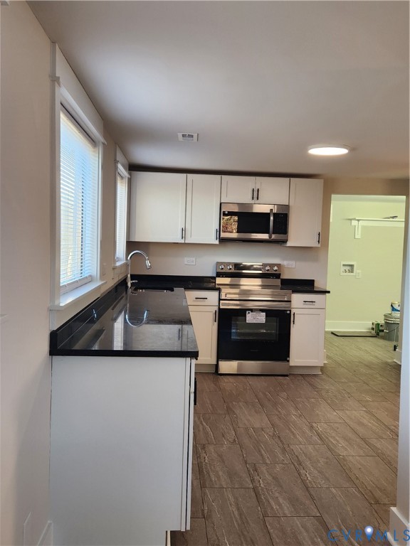 Kitchen featuring white cabinetry, dark stone countertops, stainless steel appliances, and wood-finish flooring