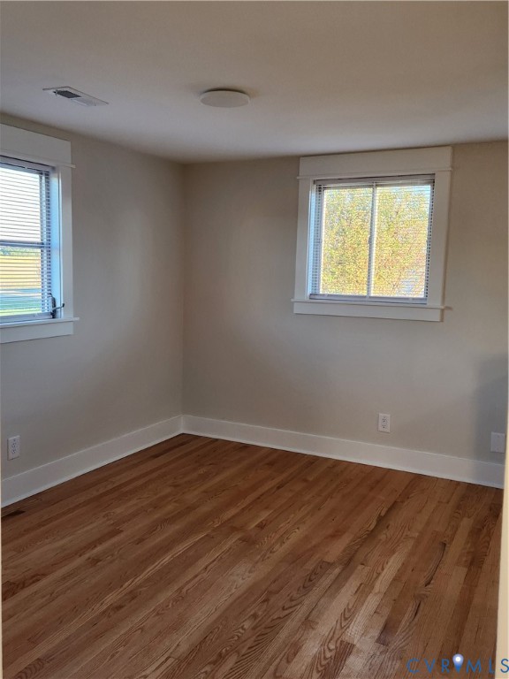 Room featuring natural wood-finish flooring, neutral wall paint, and dual windows with wide-profile white trim