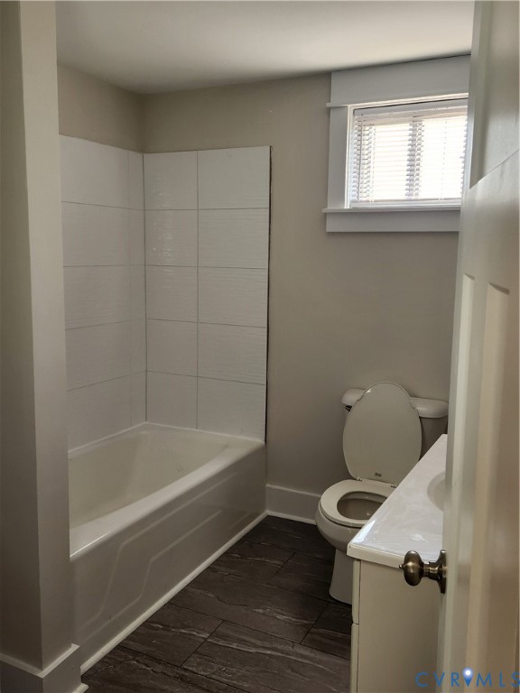 Bathroom featuring wood-finish tile flooring, a white porcelain tub with integrated tile surround, a crisp white vanity, and a window with white trim