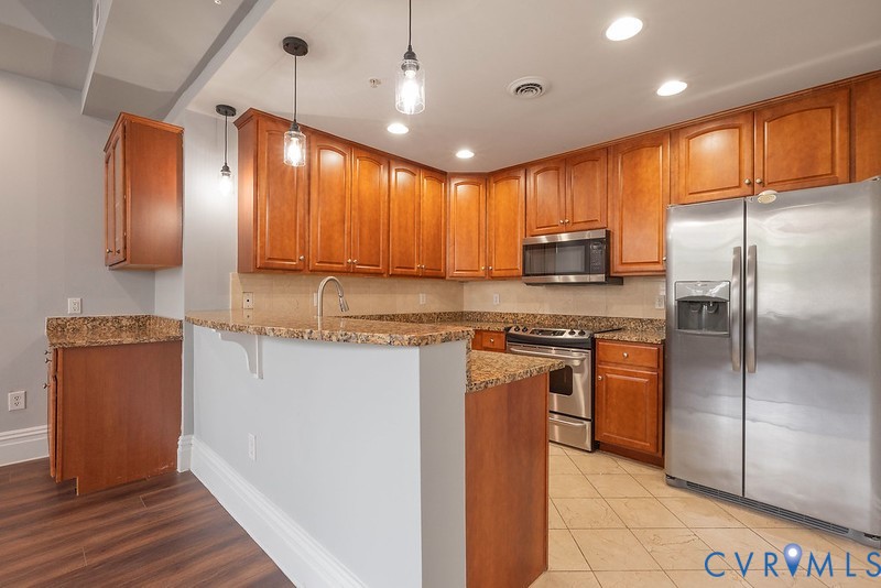 Kitchen featuring wood cabinetry, stone countertops, stainless steel appliances, pendant lighting, and tiled flooring