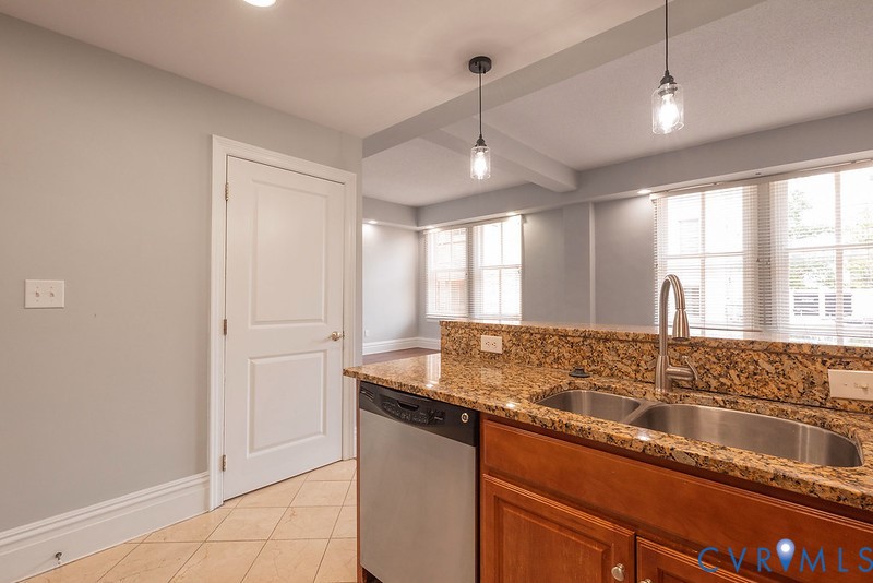 Kitchen featuring natural stone countertops, stainless steel undermount double-basin sink, high-arc faucet, wood cabinetry, and pendant lighting