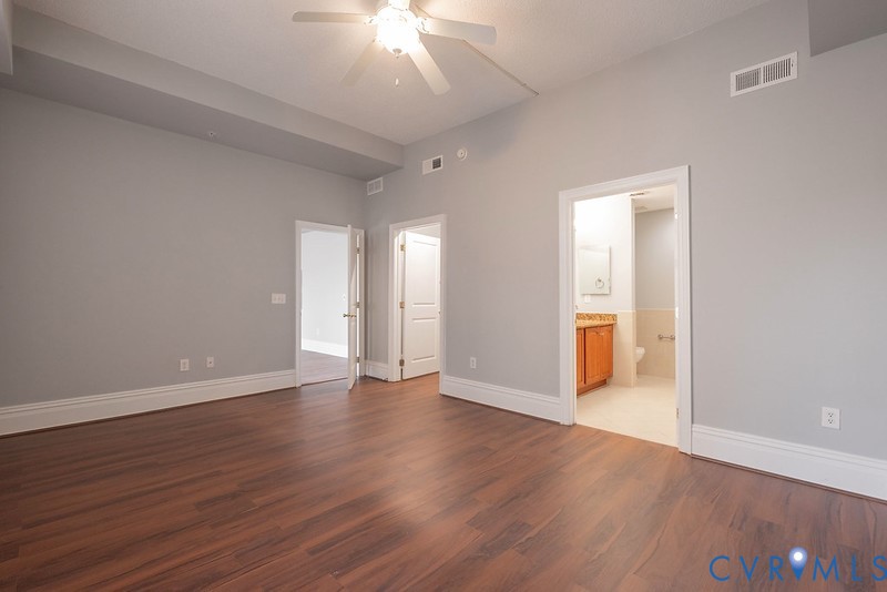 Interior room featuring tray ceilings, a ceiling fan, wood-finish flooring, and multi-panel interior doors