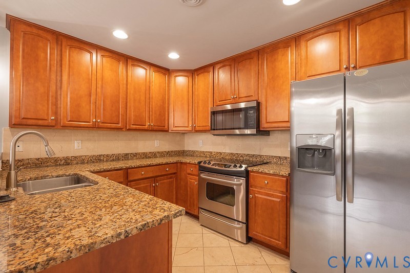 Kitchen featuring wood cabinetry, stone countertops, stainless steel appliances, a built-in microwave, and tile flooring