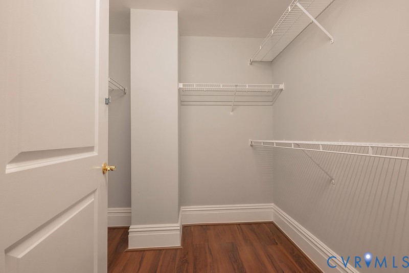 Walk-in closet featuring wood-finish flooring, white paneled door with brass-tone hardware, and tiered wire shelving