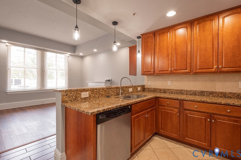 Kitchen featuring wood cabinetry, stone-surface countertops, tile backsplash, stainless steel dishwasher, and pendant lighting