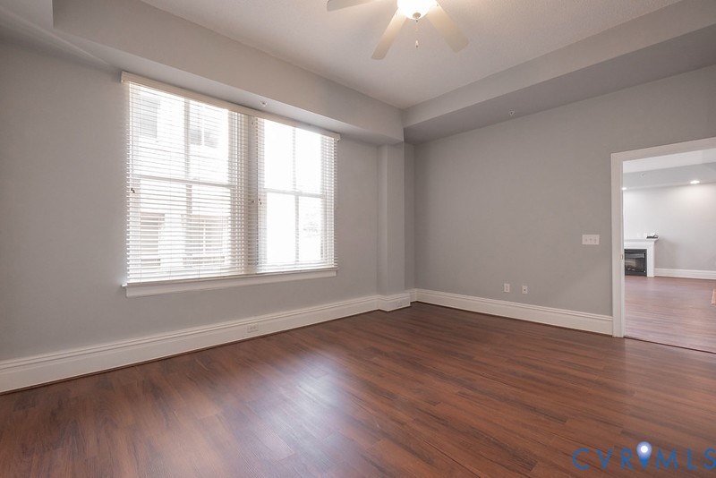 Room featuring wood-finish flooring, recessed tray ceiling with an integrated ceiling fan, and large windows with horizontal blinds