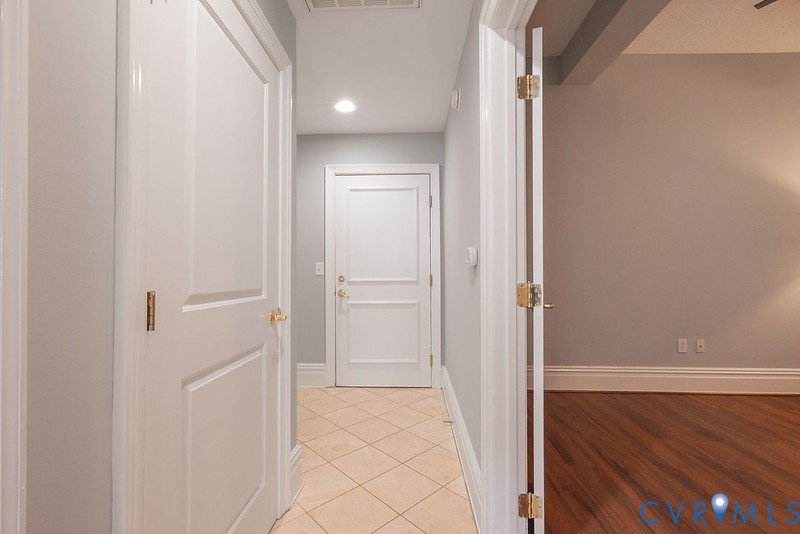 Entryway featuring neutral-toned tile flooring, recessed lighting, and multi-panel interior doors with brass hardware, complemented by wood-finish flooring in the adjacent room