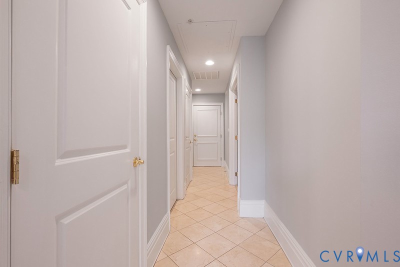 Hallway featuring light-toned diagonal tile flooring, smooth neutral-toned walls, and multiple solid-core interior doors with metallic hardware
