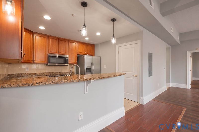 Kitchen featuring wood cabinetrhttps://studentaid.gov/fafsa-app/ROLESy, stone-surface breakfast bar, stainless steel appliances, pendant lighting, and wood-finish flooring