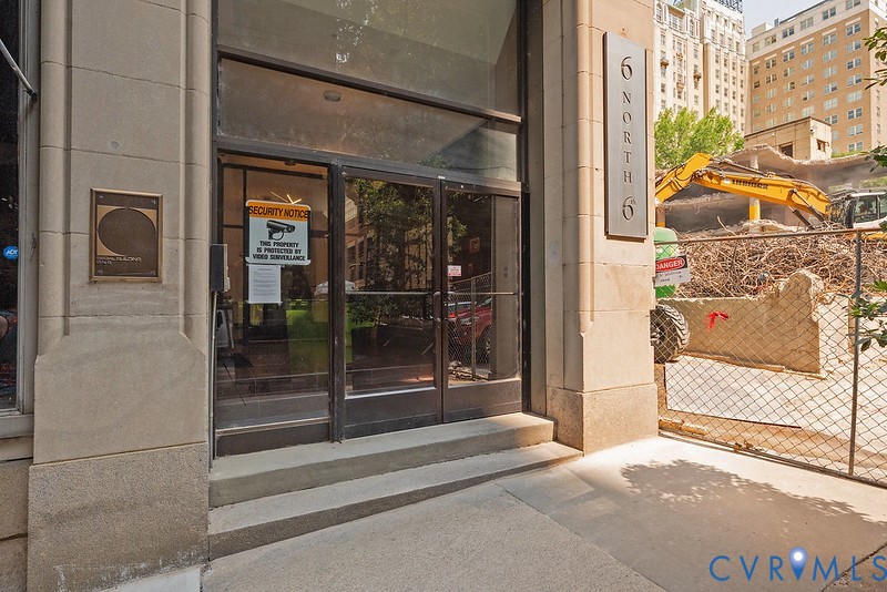 Stone-clad building facade featuring a glass entry door, multi-pane transom window, and prominent metallic building signage Stone-clad building facade featuring a glass entry door, multi-pane transom window, and prominent metallic building signage
