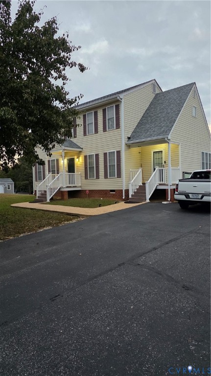 Two-story exterior featuring light-colored siding, dark shutters, an asphalt shingled roof, dual elevated entryways with white railing, and a paved driveway Two-story exterior featuring light-colored siding, dark shutters, an asphalt shingled roof, dual elevated entryways with white railing, and a paved driveway