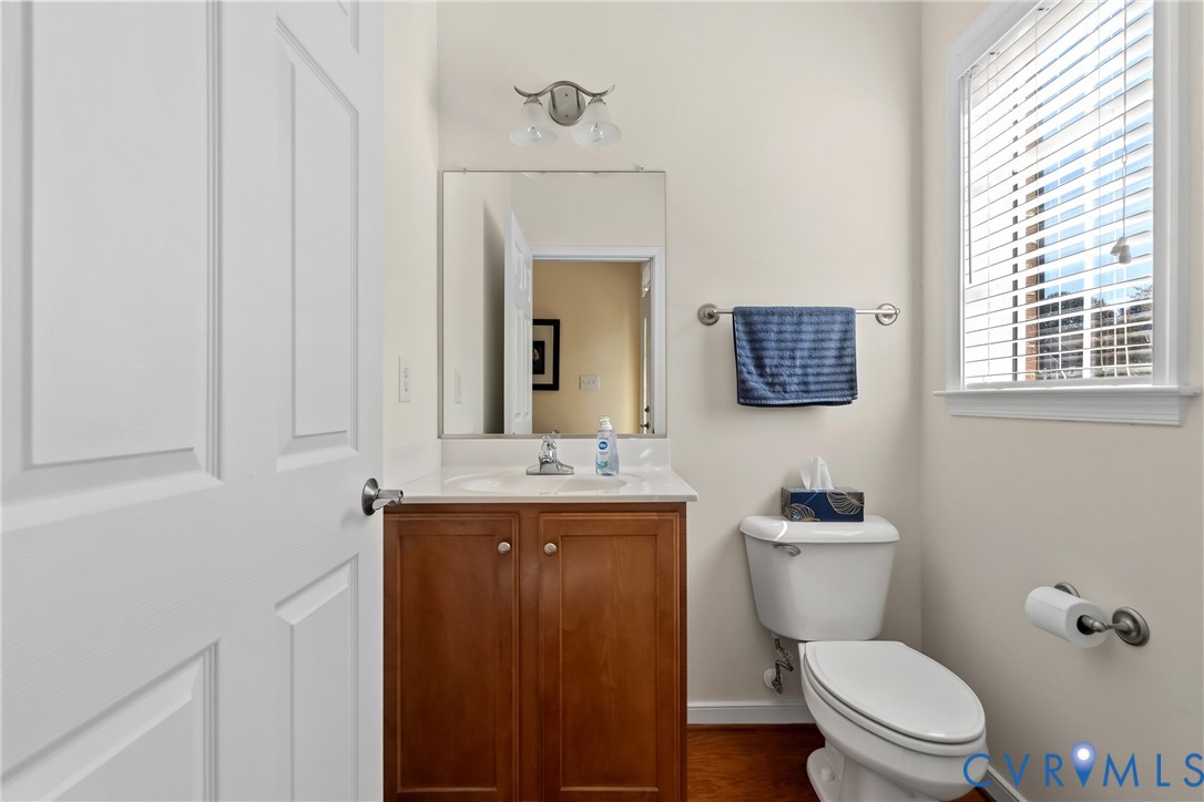 Wood-finish cabinetry, white countertop with integrated sink, polished metal hardware, wall-mounted mirror with dual-light fixture, and wood-finish flooring