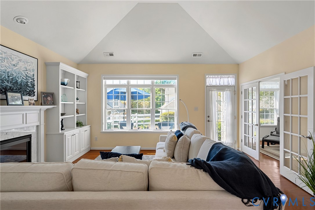 Vaulted ceiling, built-in cabinetry, wood-finish flooring, gas fireplace with white mantle, and glass-paneled French doors Vaulted ceiling, built-in cabinetry, wood-finish flooring, gas fireplace with white mantle, and glass-paneled French doors