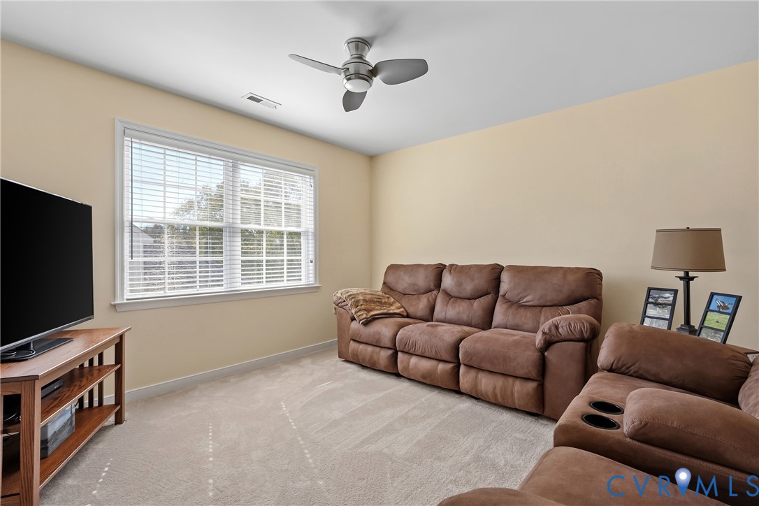 Neutral-toned room featuring wall-to-wall carpeting, a large double-hung window, and a brushed nickel ceiling fan with integrated light