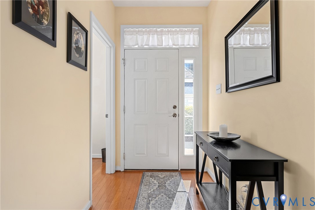 Light filled entryway featuring a white six-panel door, vertical sidelight window, overhead transom window, and wood-finish flooring Light filled entryway featuring a white six-panel door, vertical sidelight window, overhead transom window, and wood-finish flooring