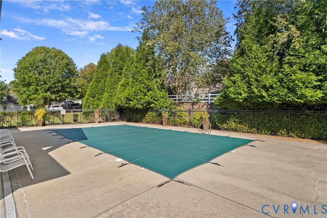 Community In-ground pool, concrete pool deck, and perimeter black metal fencing surrounded by mature evergreen trees