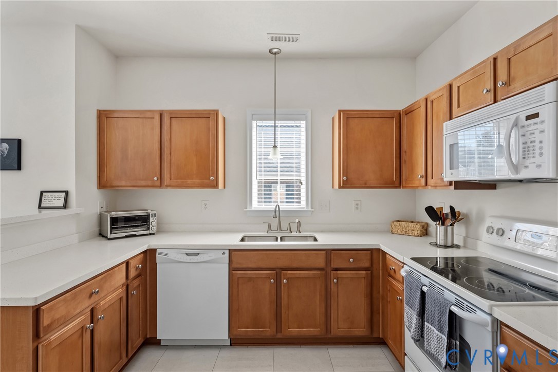 Kitchen featuring natural wood cabinetry, solid-surface countertops, dual-basin stainless steel sink, LVT flooring, and integrated white appliances Kitchen featuring natural wood cabinetry, solid-surface countertops, dual-basin stainless steel sink, LVT flooring, and integrated white appliances