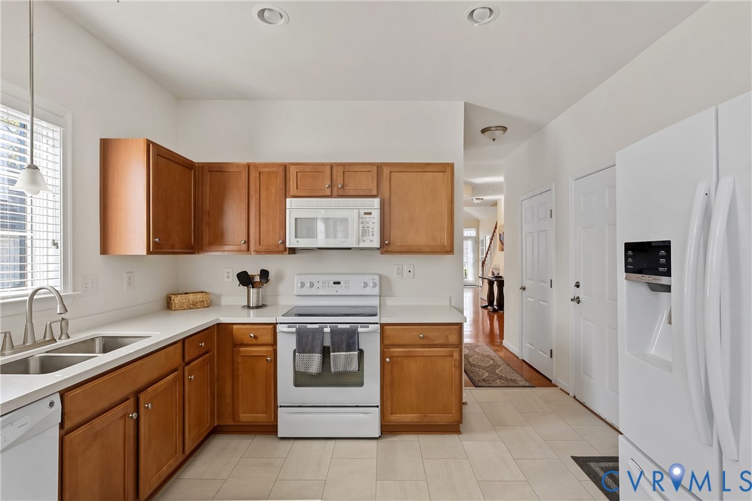 Kitchen featuring wood cabinetry, white countertops, a double-basin stainless steel sink with a high-arch faucet, white appliances, and LVT flooring Kitchen featuring wood cabinetry, white countertops, a double-basin stainless steel sink with a high-arch faucet, white appliances, and LVT flooring