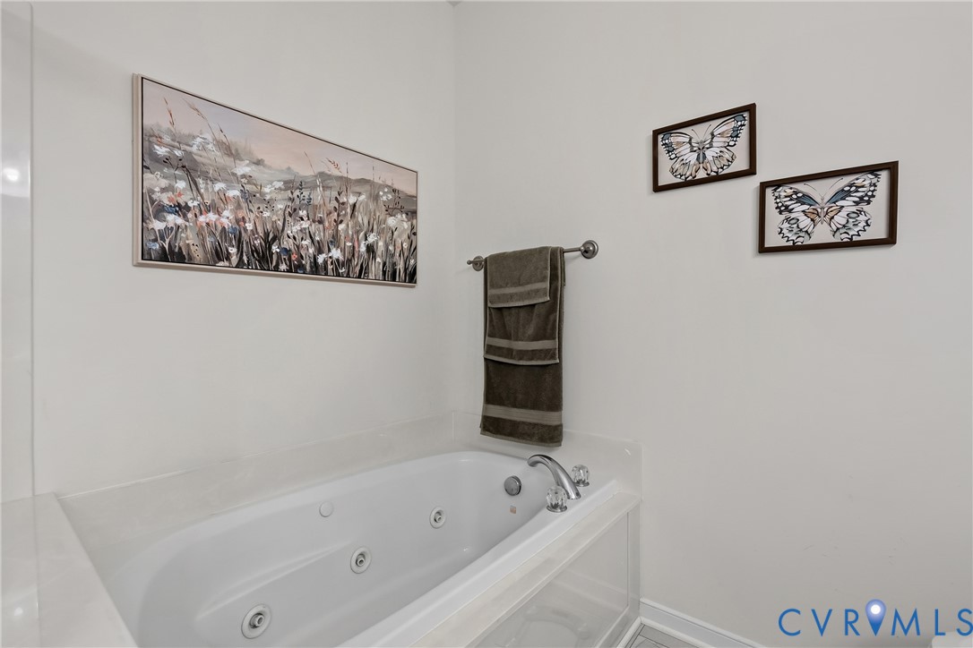 Jetted soaking tub featuring a deck-mounted chrome faucet, surrounding paneling, and an integrated towel bar