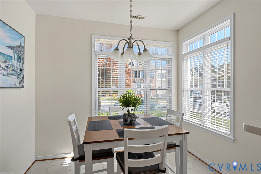 Sun-drenched dining area featuring large windows with integrated blinds, LVT flooring, and a multi-arm pendant light fixture Sun-drenched dining area featuring large windows with integrated blinds, LVT flooring, and a multi-arm pendant light fixture