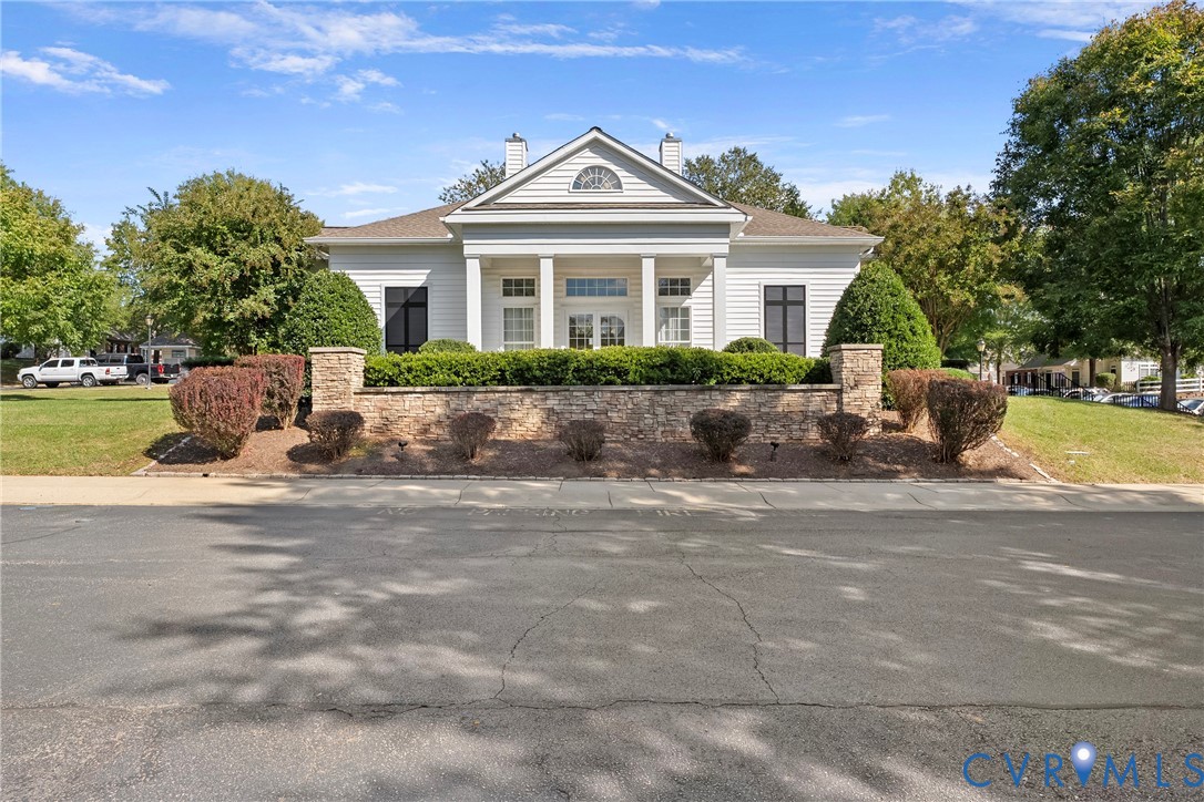 Clubhouse with classical exterior featuring a gabled roofline, prominent white columns, horizontal siding, masonry retaining wall, and arched transom window details