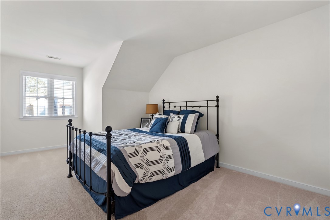 Neutral-toned wall-to-wall carpeting, vaulted ceiling with architectural slope, and a window with white casing