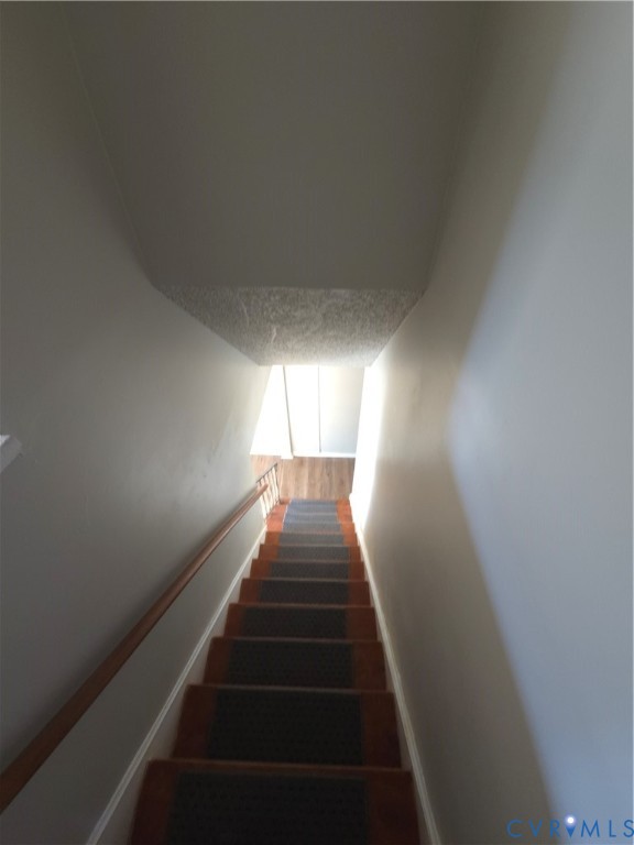 Staircase featuring wood-finish treads, central carpeted runners, and a wall-mounted wooden handrail