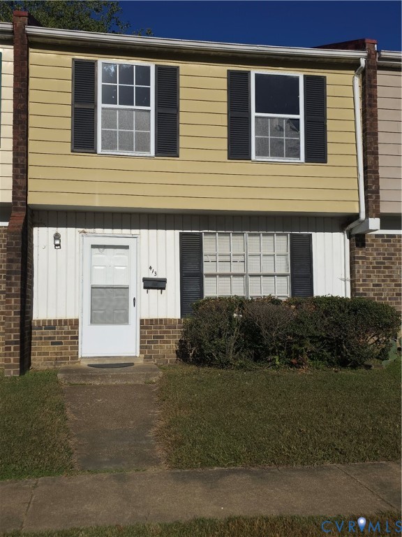 Exterior facade featuring horizontal siding, brick masonry detailing, decorative window shutters, and a multi-pane front entry door