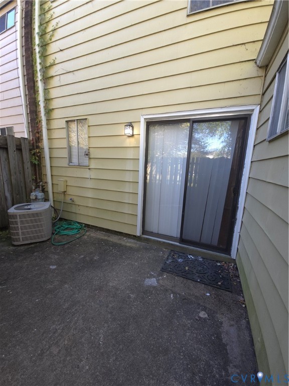 Exterior patio area featuring concrete hardscaping, horizontal siding, and a sliding glass door with external wall-mounted lighting Exterior patio area featuring concrete hardscaping, horizontal siding, and a sliding glass door with external wall-mounted lighting