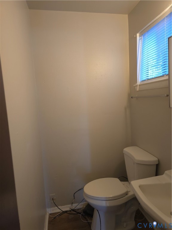 Neutral-toned walls, pedestal sink, white porcelain toilet, and horizontal window blinds Neutral-toned walls, pedestal sink, white porcelain toilet, and horizontal window blinds