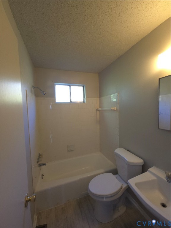 Bathroom featuring a porcelain tub with tile surround, wall-mounted shower head, ceramic sink with chrome hardware, and wood-finish flooring