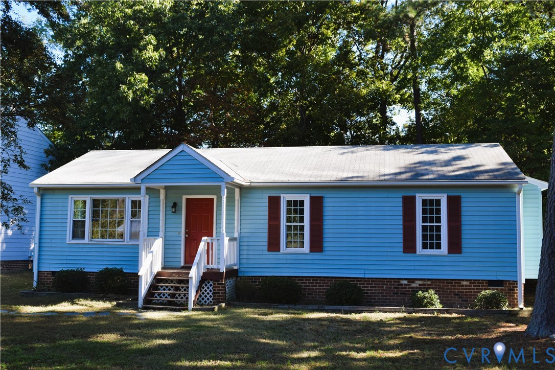 Single-story residence featuring horizontal siding, brick masonry foundation, covered front porch with white railing, and decorative window shutters